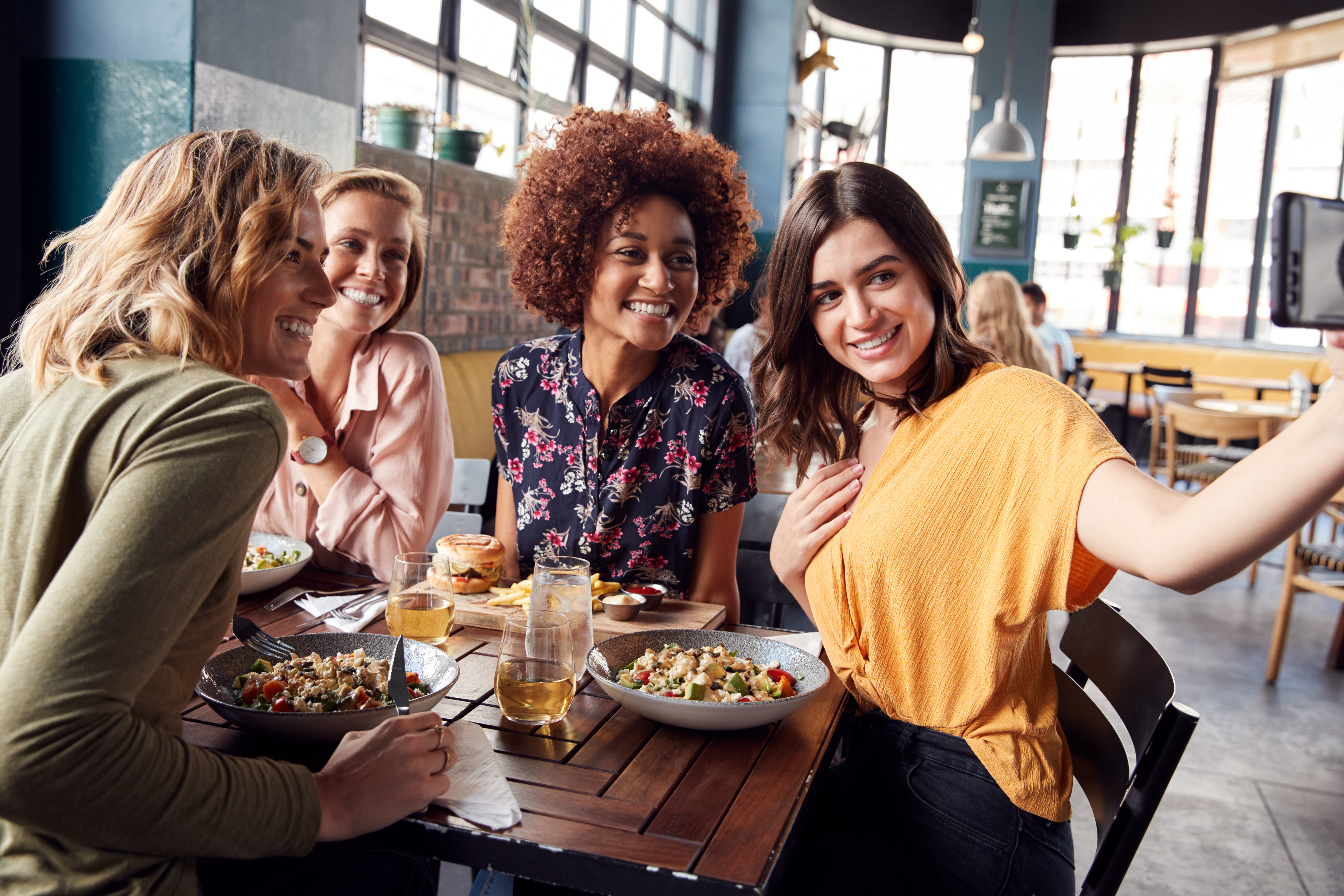 Four Young Female Friends Meeting For Drinks And Food Posing For Selfie In Restaurant